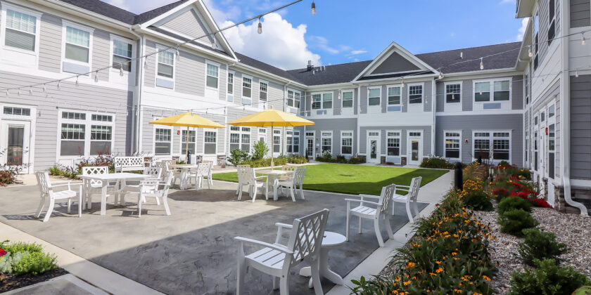 Patio area outside of the senior living residences at Traditions at Camargo with white lounge chairs and yellow umbrellas in patio tables