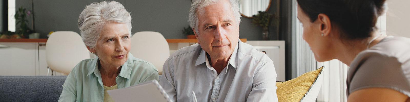 A senior man and woman sitting on a couch across from a woman talking to them about senior living and insurance eligibility