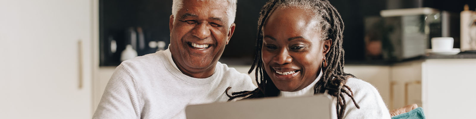 A senior man and woman sitting together on a couch looking down at a laptop